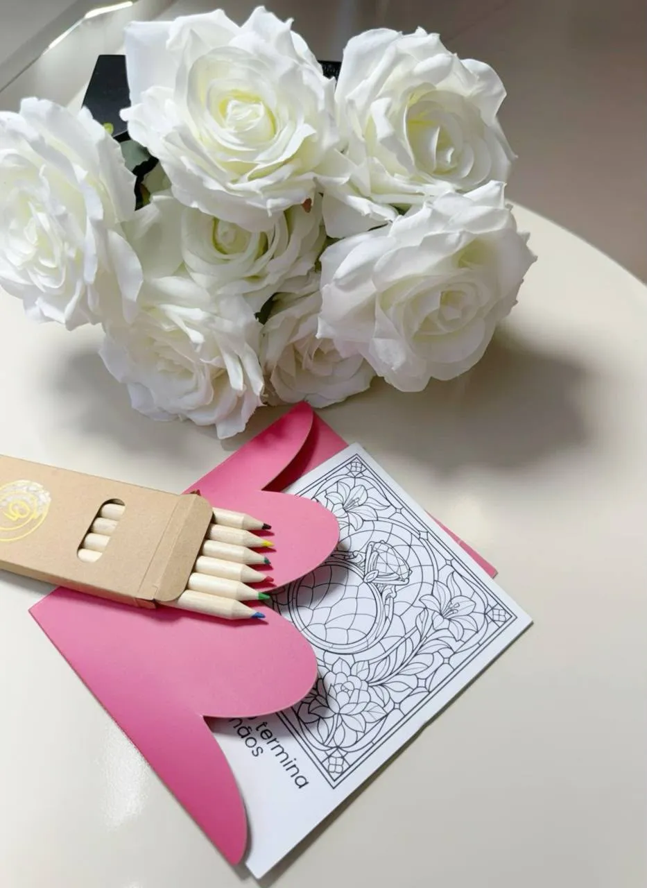Cartão de colorir da coleção Tessalia dentro do envelope rosa, ao lado de uma caixinha de lápis de cor