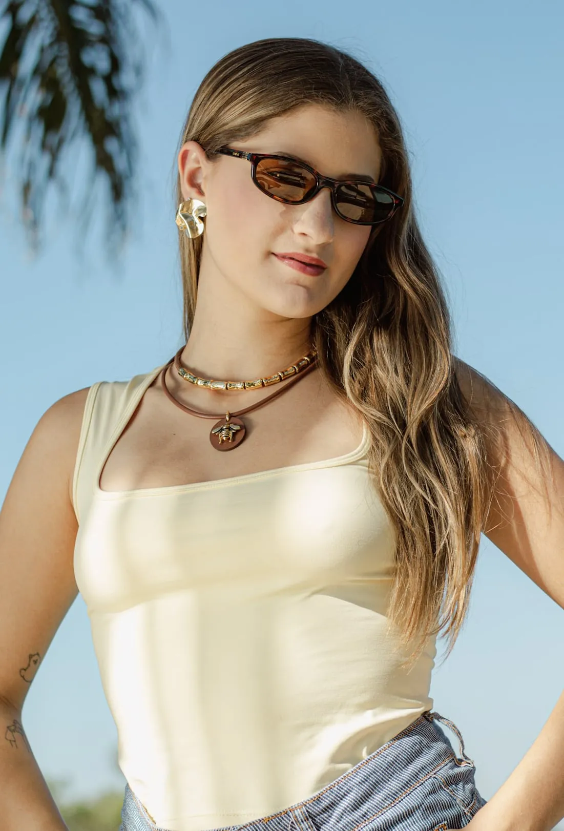 Modelo sorrindo ao ar livre, usando óculos de sol e colar
