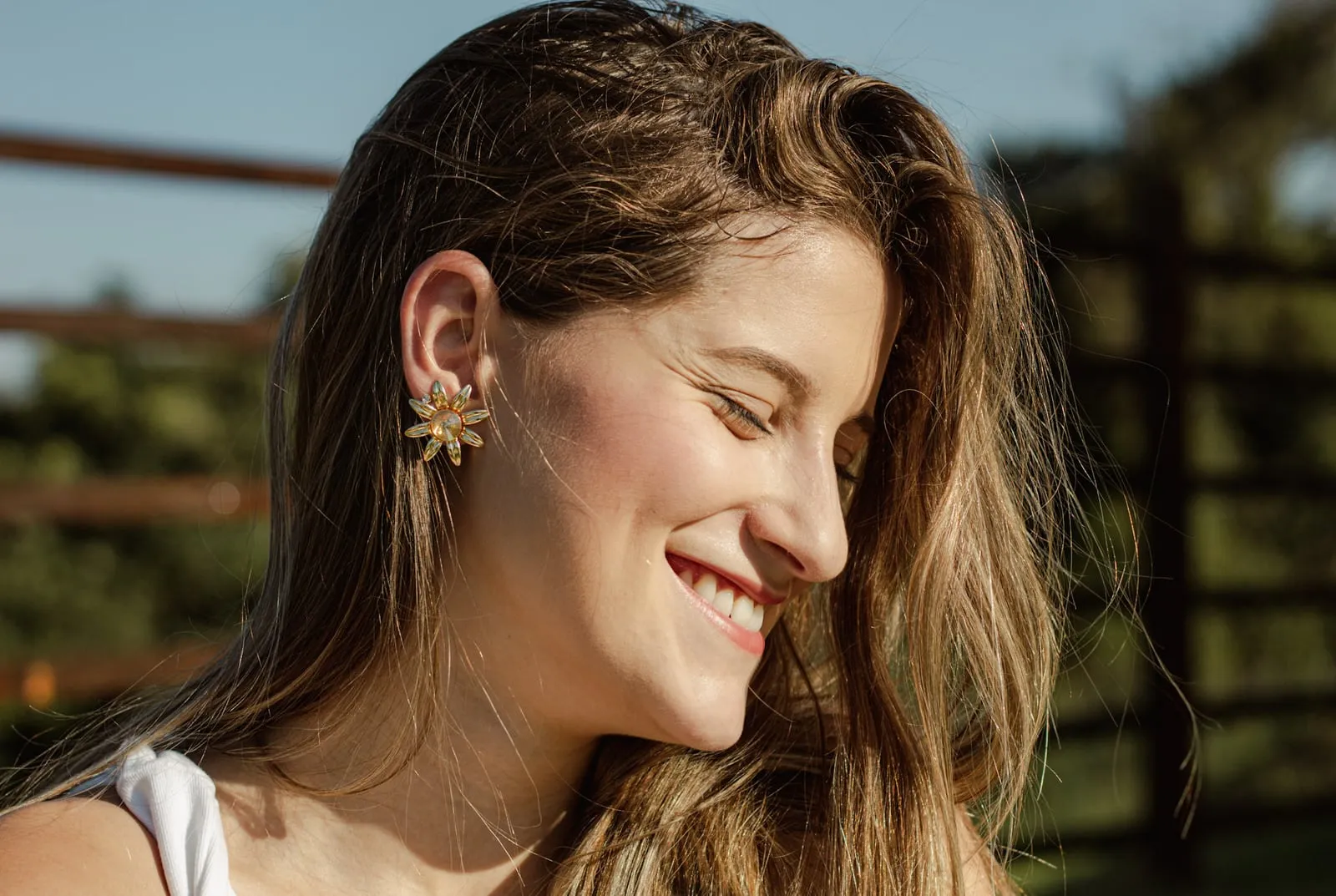 Perfil de modelo sorrindo, brinco em destaque contra o céu