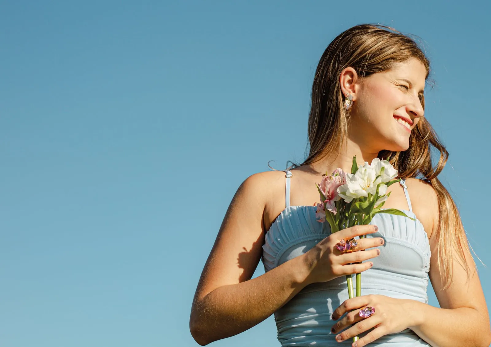 Modelo ao ar livre segurando um buquê de flores, vestido azul claro